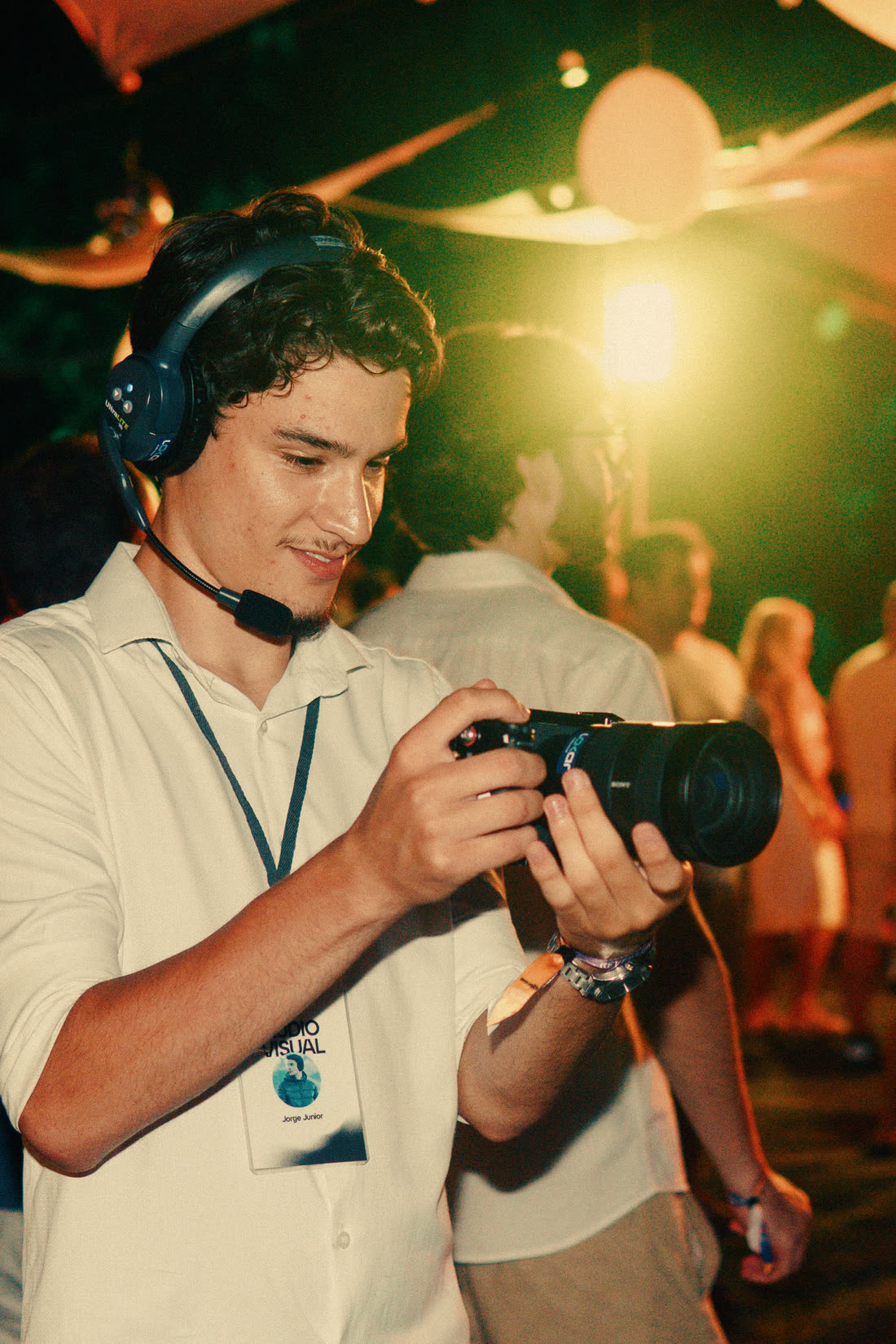 Jorge Jr de fones, com a câmera na mão, filmando uma festa à noite
